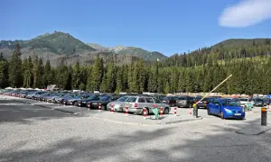 Parking pod Morskim Okiem, pełen samochodów, z górami i lasem w tle.