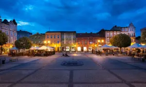 Wieczorny rynek w Kościerzynie, z oświetlonymi kamienicami i ogródkami restauracyjnymi.