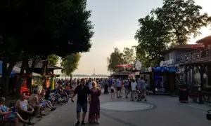 Tłum ludzi spaceruje promenadą w Skorzęcinie, korzystając z licznych atrakcji i letniej atmosfery nad jeziorem.