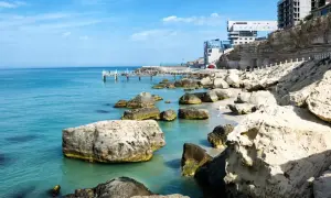 Brzeg największego morza w Europie, z turkusową wodą, kamienistą plażą i nowoczesnymi budynkami na klifie.