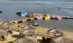 Słoneczna plaża Skorochów z parasolami, leżakami i kolorowymi łódkami wodnymi przy drewnianym pomoście.
