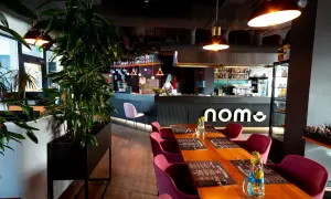 Elegancka restauracja z drewnianymi stołami, bordowymi krzesłami i barem z logo "nome".