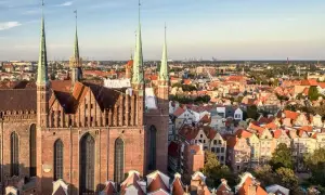 Widok na Bazylikę Mariacką i urokliwe kamienice Gdańska Stare Miasto. Dachy w odcieniach czerwieni i pomarańczy tworzą malowniczy krajobraz.