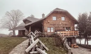 Drewniany dom z kamienną podstawą, kamienista ścieżka i płot. Mglisty dzień dodaje uroku temu miejscu, które oferuje liczne laskowa atrakcje.