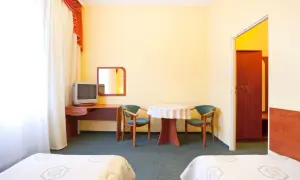 Pokój hotelowy z dwoma łóżkami, biurkiem z telewizorem, stolikiem z krzesłami i szafą.