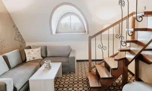 Przytulny salon z kanapą i stolikiem, drewniane schody i okno z widokiem na góry. Idealne miejsce na relaks i odkrywanie kocierz atrakcje.