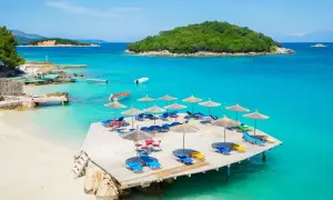 Rajska plaża w Albanii. Turkusowe morze, piaszczysta plaża, drewniany taras z leżakami i parasolami.