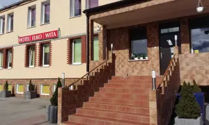 Wejście do hotelu Elko Elbląg. Schody prowadzą do drzwi, a nad nimi widnieje czerwony szyld.