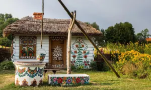 Malowana chata z łubą i studnią, ozdobiona kwiatami. Warto zobaczyć Zalipie i okolice, by podziwiać ludową sztukę.