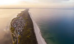 Z lotu ptaka widać malowniczą plażę w Chałupach, z domkami i lasem po jednej stronie, a spokojnym morzem po drugiej.