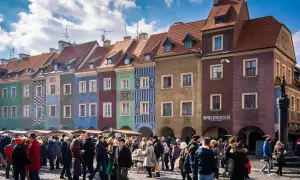 Kolorowe kamienice na Starym Rynku w Poznaniu. Tłum ludzi spaceruje po bruku. Idealne miejsce, by poczuć atmosferę miasta, gdy już wiesz, jak dojechać z dworca głównego w Poznaniu na stary rynek.