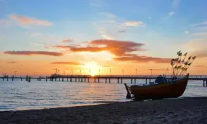 Łódź na plaży o zachodzie słońca, z molo w tle. Idealne miejsce, by zapytać, gdzie najbliżej nad morze z łodzi.