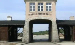Brama obozu Gross-Rosen z napisem "Arbeit Macht Frei". W oddali krzyż.