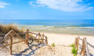 Drewniane schody prowadzą na piaszczystą plażę w Lubiatowie. Spokojne morze i błękitne niebo zapraszają do odpoczynku.