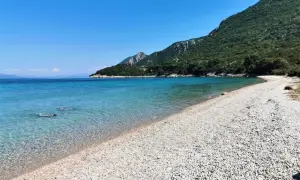 Chorwacja jakie morze? Turkusowa woda, kamienista plaża i zielone wzgórza. Dwie osoby pływają w krystalicznie czystej wodzie.