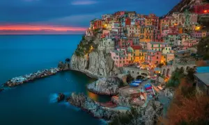 Kolorowe domy Cinque Terre w **Włoszech** wznoszą się nad skalistym wybrzeżem. **Morze** Liguryjskie lśni w blasku zachodzącego słońca.