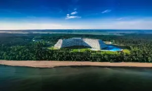 Gołębiewski nad morzem, z basenem i plażą, otoczony lasem, na tle wiatraków i błękitnego nieba.