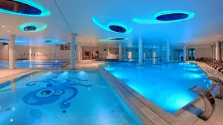 Nowoczesny aquapark w Ustce z basenami, jacuzzi i kolorowym oświetleniem. Na dnie jednego z basenów widnieje mozaika z ośmiornicą.