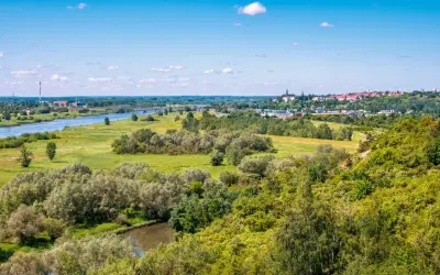 Krajobraz z rzeką, zielonymi wzgórzami porośniętymi drzewami i miastem w oddali.