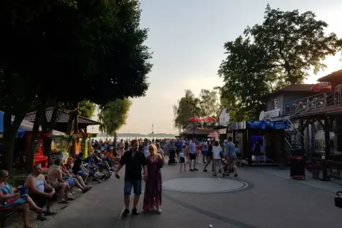 Tłum ludzi spaceruje promenadą w Skorzęcinie, korzystając z licznych atrakcji i letniej atmosfery nad jeziorem.