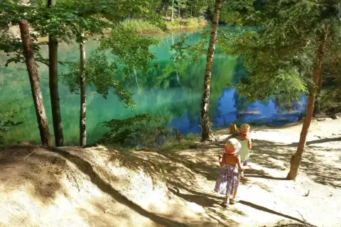 Dwie dziewczynki w słomkowych kapeluszach idą ścieżką nad turkusowe jezioro. Idealne miejsce, gdzie w góry z dzieckiem 2 letnim na spacer.