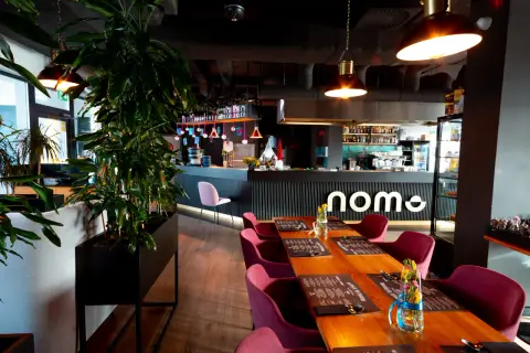 Elegancka restauracja z drewnianymi stołami, bordowymi krzesłami i barem z logo "nome".