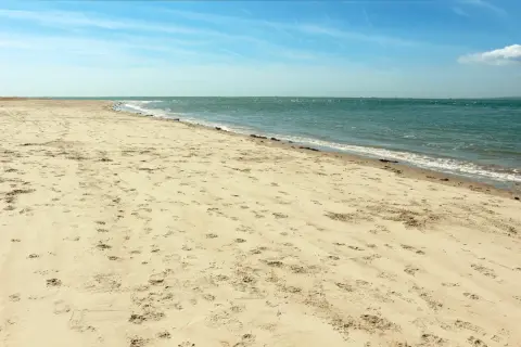Pusta plaża Ulinia z licznymi śladami na piasku, spokojne morze i błękitne niebo.