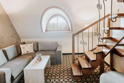 Przytulny salon z kanapą i stolikiem, drewniane schody i okno z widokiem na góry. Idealne miejsce na relaks i odkrywanie kocierz atrakcje.