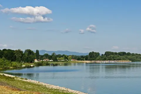 Spokojne jezioro otmuchowskie z łodziami przy brzegu, otoczone zielenią. Idealne miejsce na wypoczynek i odkrywanie atrakcji.