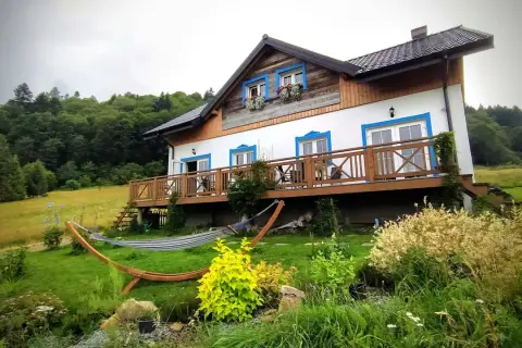 Dom z werandą i hamakiem w otoczeniu zieleni, idealne miejsce na wypoczynek w Bieszczadach.