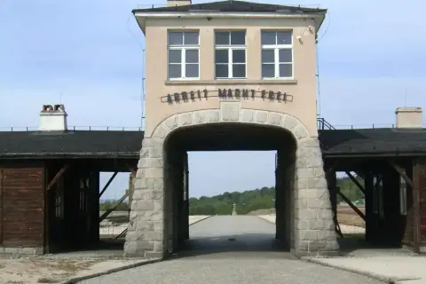 Brama obozu Gross-Rosen z napisem "Arbeit Macht Frei". W oddali krzyż.