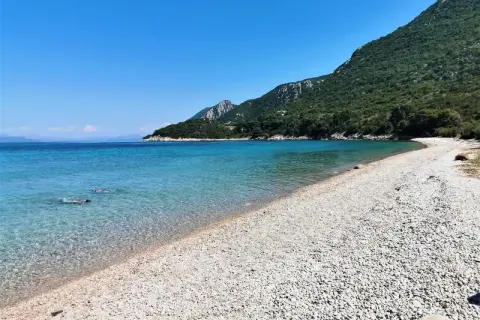 Chorwacja jakie morze? Turkusowa woda, kamienista plaża i zielone wzgórza. Dwie osoby pływają w krystalicznie czystej wodzie.