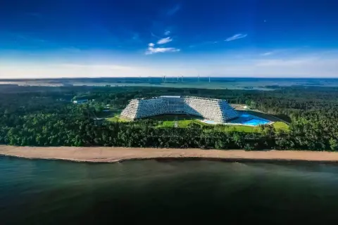 Gołębiewski nad morzem, z basenem i plażą, otoczony lasem, na tle wiatraków i błękitnego nieba.