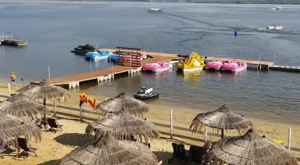 Słoneczna plaża Skorochów z parasolami, leżakami i kolorowymi łódkami wodnymi przy drewnianym pomoście.