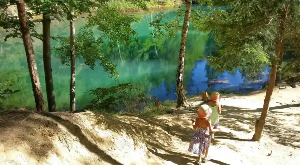 Dwie dziewczynki w słomkowych kapeluszach idą ścieżką nad turkusowe jezioro. Idealne miejsce, gdzie w góry z dzieckiem 2 letnim na spacer.