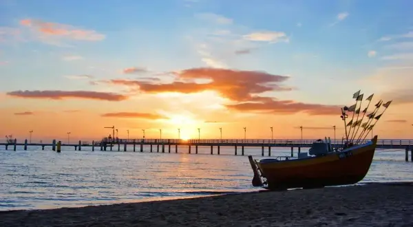 Łódź na plaży o zachodzie słońca, z molo w tle. Idealne miejsce, by zapytać, gdzie najbliżej nad morze z łodzi.
