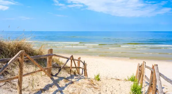 Drewniane schody prowadzą na piaszczystą plażę w Lubiatowie. Spokojne morze i błękitne niebo zapraszają do odpoczynku.