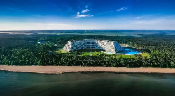Gołębiewski nad morzem, z basenem i plażą, otoczony lasem, na tle wiatraków i błękitnego nieba.
