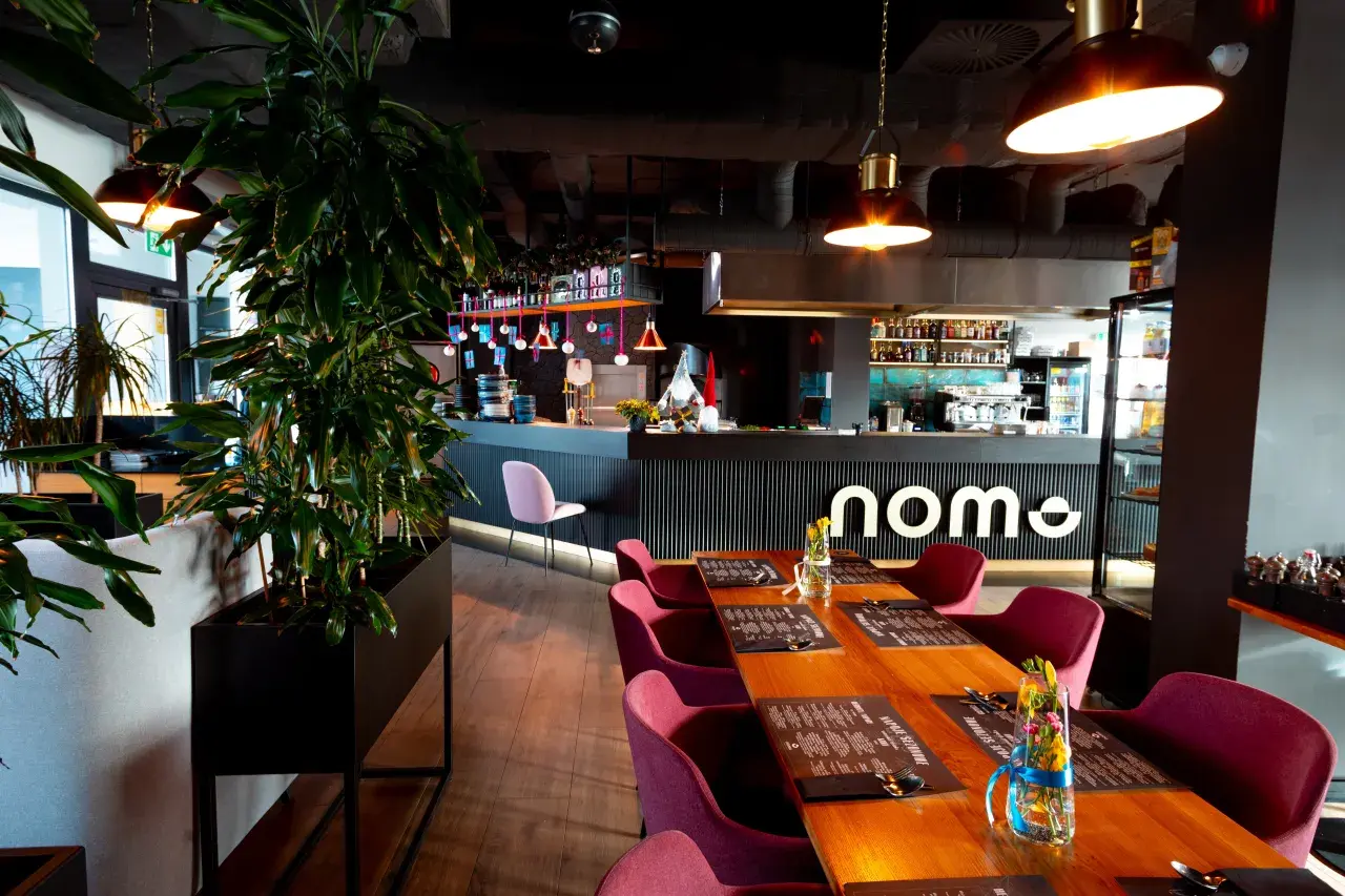 Elegancka restauracja z drewnianymi stołami, bordowymi krzesłami i barem z logo "nome".