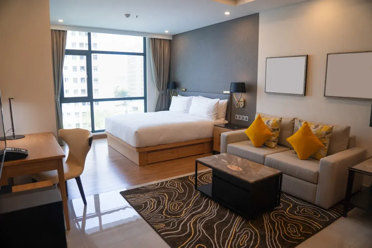 Nowoczesny pokój hotelowy z łóżkiem, sofą i biurkiem, widok z okna na miasto.