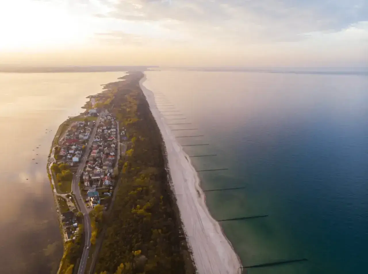 Z lotu ptaka widać malowniczą plażę w Chałupach, z domkami i lasem po jednej stronie, a spokojnym morzem po drugiej.