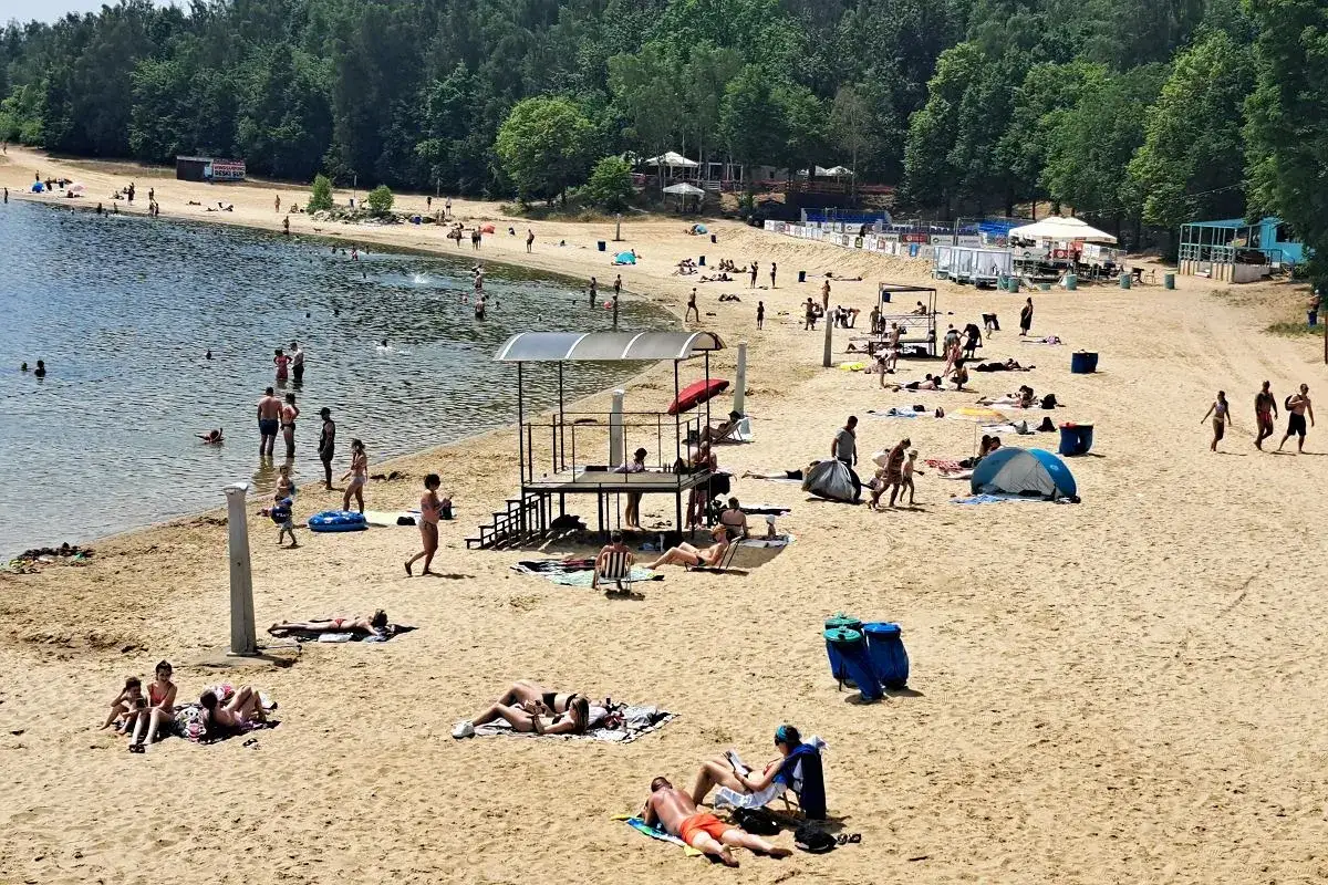 Ludzie odpoczywają i kąpią się na piaszczystej plaży Skorochów. Woda jest spokojna, a na brzegu widać leżaki i parasole.