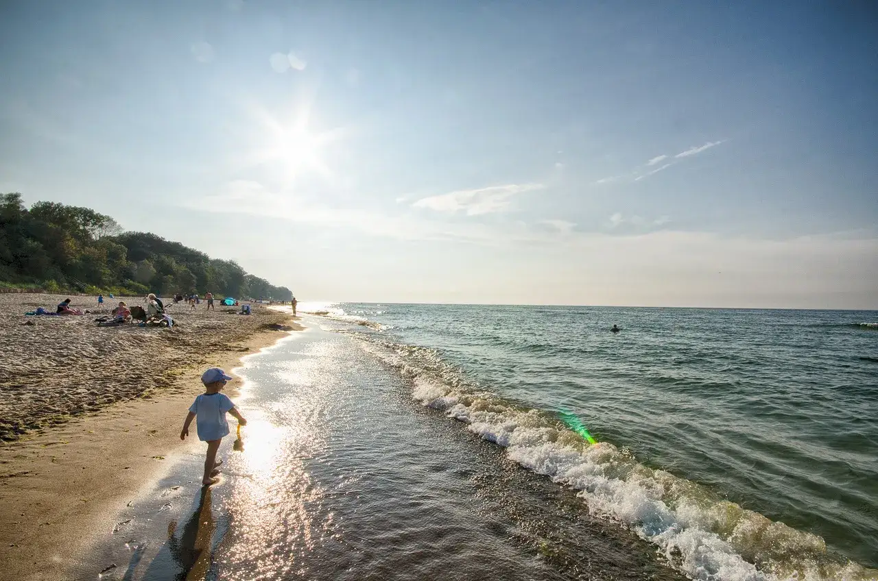 Dziecko bawi się na plaży w Gąskach, ciesząc się słońcem i falami. To idealne miejsce na rodzinne atrakcje dla dzieci.