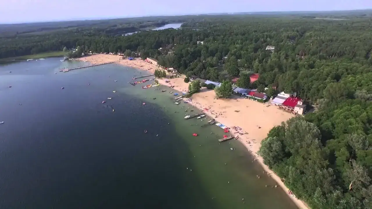 Skorzęcin atrakcje: plaża pełna ludzi, kąpielisko, pomost, łódki i rowery wodne. Las otacza jezioro.
