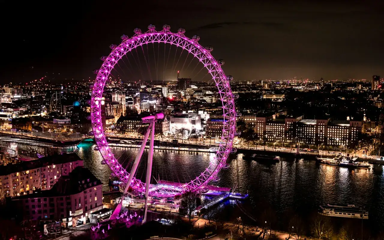 Nocny Londyn z różowym London Eye. Jego imponująca london eye wysokość robi wrażenie na tle rozświetlonego miasta i Tamizy.