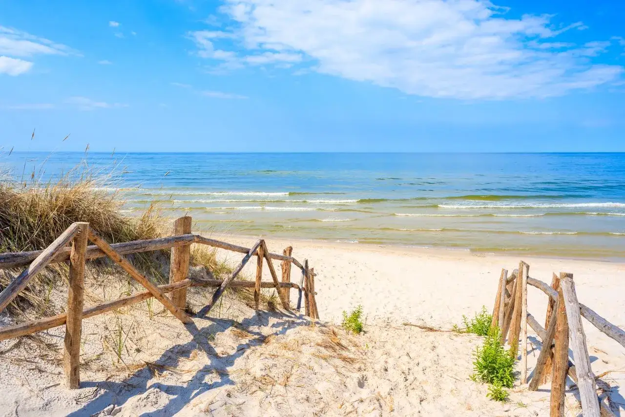 Drewniane schody prowadzą na piaszczystą plażę w Lubiatowie. Spokojne morze i błękitne niebo tworzą idealny krajobraz.