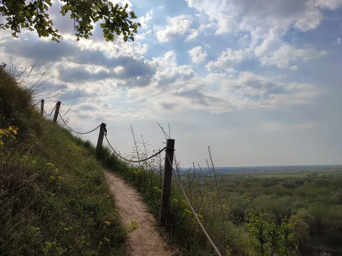 Ścieżka na zboczu, z linami zabezpieczającymi, prowadzi ku widokowi na dolinę. Góry pieprzowe ukazują swoją wysokość w krajobrazie.