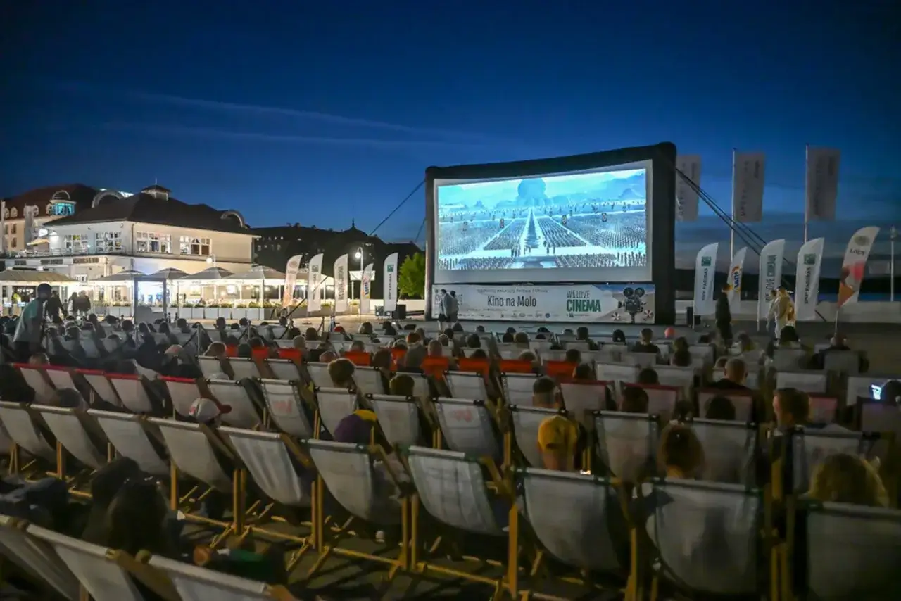 Wieczorne kino plenerowe na molo, część festiwali filmowych w Polsce. Widownia siedzi na leżakach, przed wielkim ekranem.