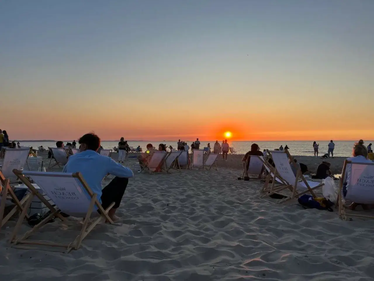 Zachód słońca na plaży w Międzyzdrojach. Ludzie siedzą na leżakach, ciesząc się wieczorem. Idealne miejsce na relaks i plażowe imprezy.