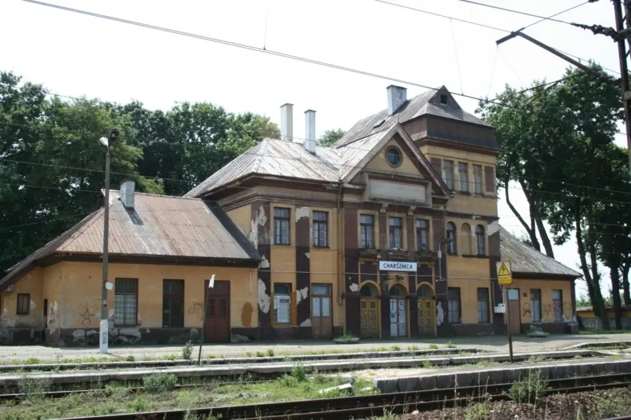 Stara, żółta stacja kolejowa w Charsznicy, zniszczona elewacja, zardzewiałe dachy, tory kolejowe.